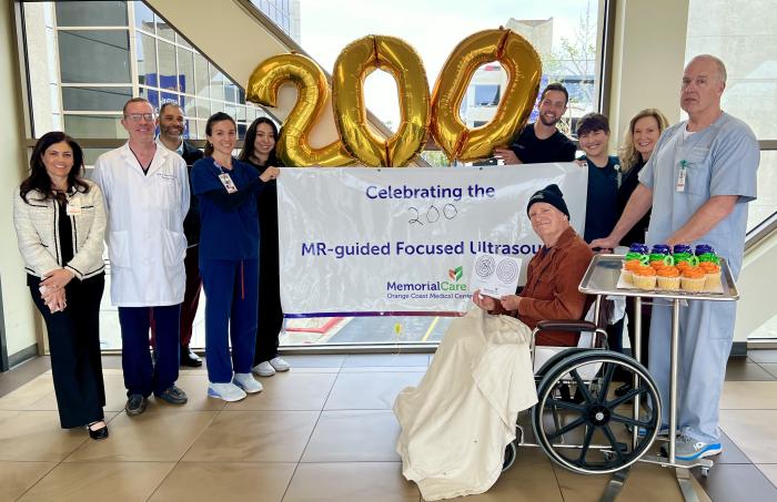 A group of doctors and nurses stand in front of a "200" balloon sign holding a banner saying "Celebrating the 200th MR-guided Focused Ultrasound. 