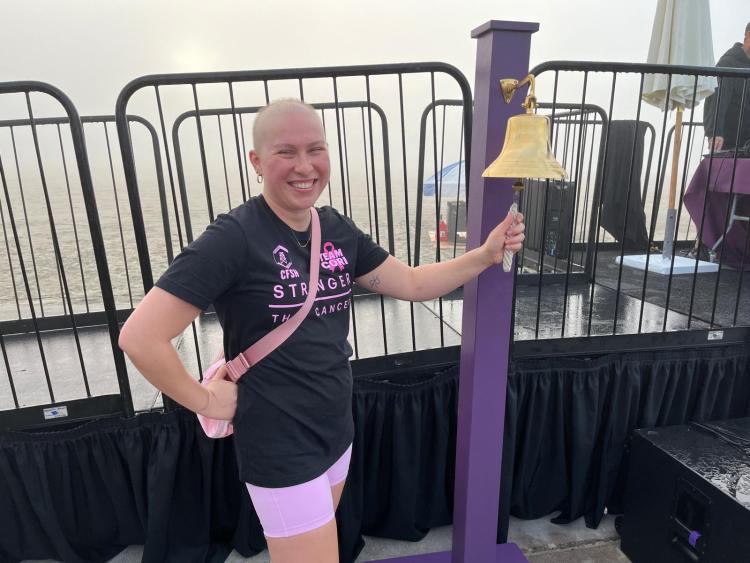 Former cancer patient Cori Reynolds rings bright bronze bell on a purple stand. 