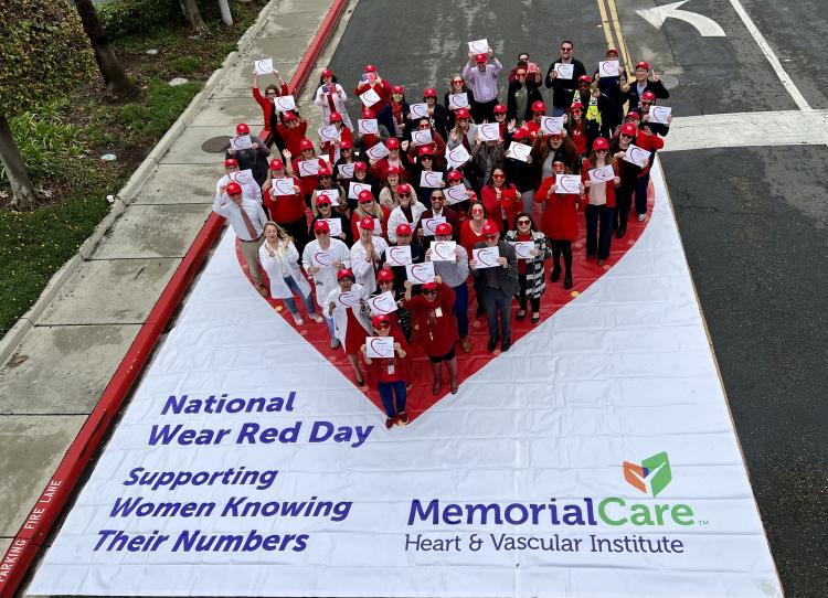 Hospital employees standing on large, heart tarp to stand in shape of large heart in the middle of two driving lanes. 