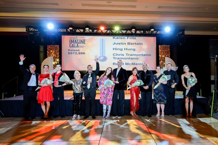 Various dancers from the Dancing for Our Stars "Imagine" Gala smile for the camera on a lit up dance floor,