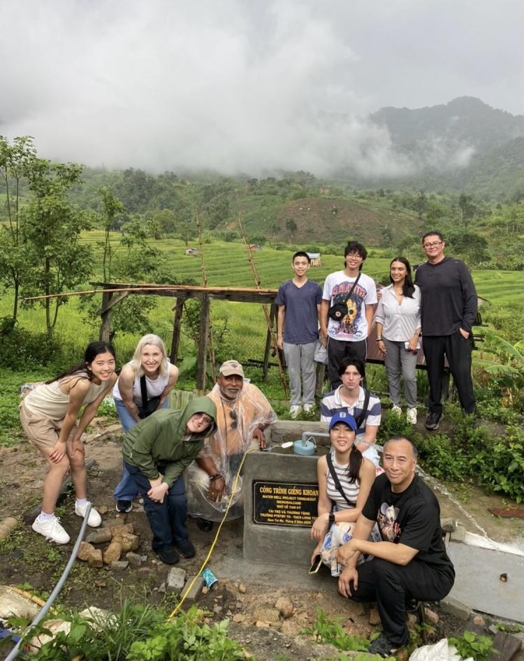 A group of volunteers from TongueOut, Dr. Trinh and Jose Juarez standing by a well they built for the community with the beautiful Thai countryside in the background. 