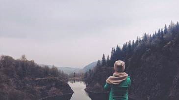 Image of the backside of a women hiking in nature. Up ahead is a view of the mountains and river.
