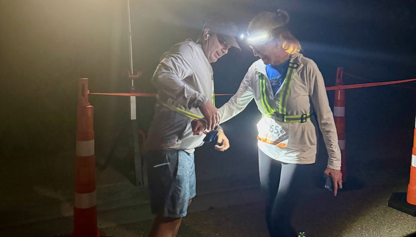 Two runners wearing headlights pass a slap bracelet in the dark. 